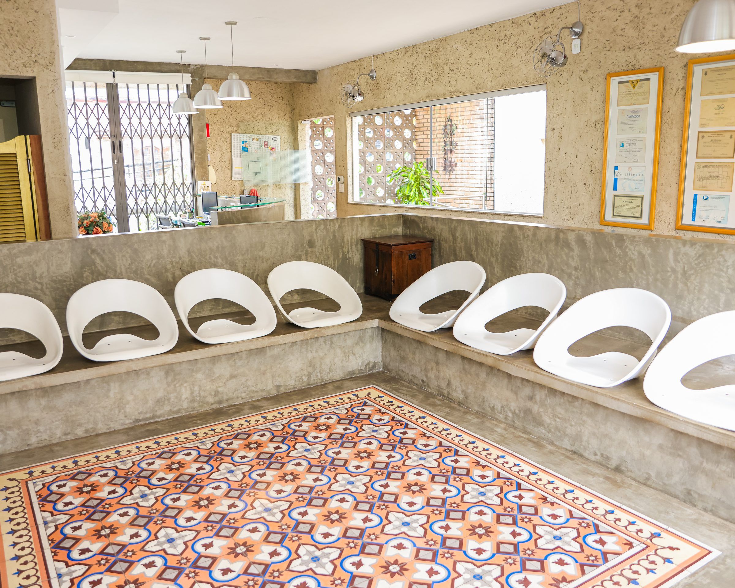 Sala de espera com poltronas brancas e piso de ladrilho hidráulico